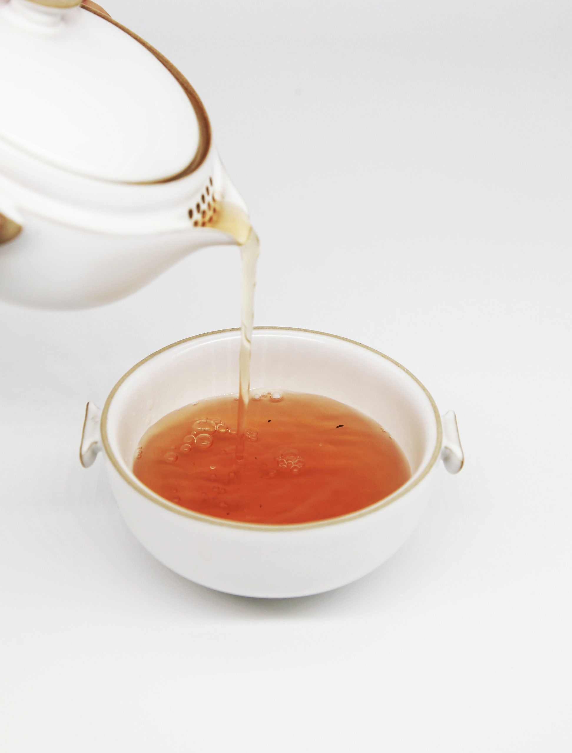pouring black tea from tea pot into tea cup